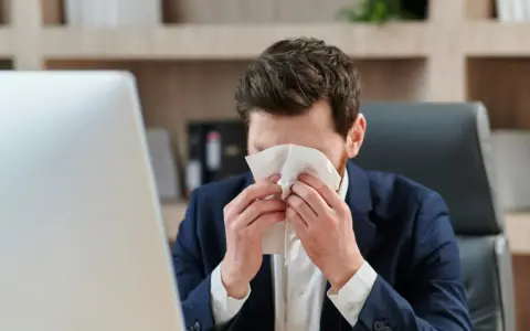 Hombre con traje se suena la nariz con un pañuelo, preocupado por un posible despido por faltar al trabajo.