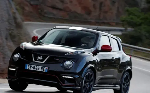 Czarny Nissan Juke Nismo z czerwonymi lusterkami i białym pasem na dachu pędzi po krętej drodze.