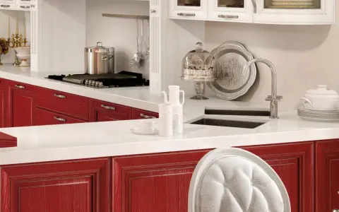 Cucina con ante rosse, piano bianco, pentola sul fornello, torta sotto campana di vetro. Okite cos'è? Un piano di lavoro resistente e bello.