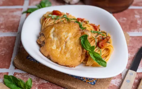 Ein paniertes Hähnchenfilet auf Spaghetti mit Tomatensoße und Basilikum. Ein Gericht, das an Piccata erinnert, aber ohne Zitrone.