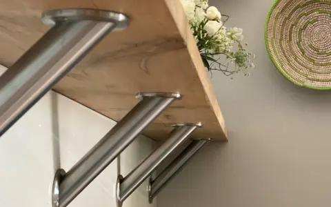 Stabile Metallwinkel befestigen die Holztheke auf der Arbeitsplatte. Ein Blumenstrauß ziert die Oberfläche.