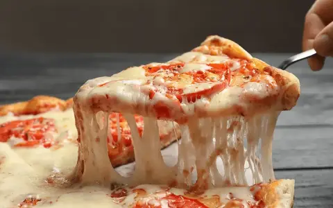 Rozciągający się, ciągnący ser na kawałku pizzy z pomidorami. Idealny przykład, jaki ser do pizzy wybrać, by uzyskać taki efekt.