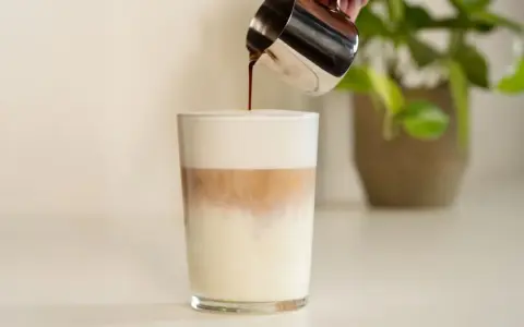 Espresso wird in ein Glas mit Milch und Milchschaum gegossen. Ein perfektes Latte Macchiato Rezept.