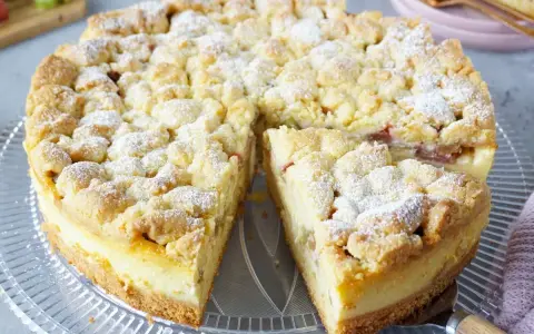 Saftiger Rhabarberkuchen mit Pudding und Streuseln, bestäubt mit Puderzucker. Ein köstlicher Genuss!