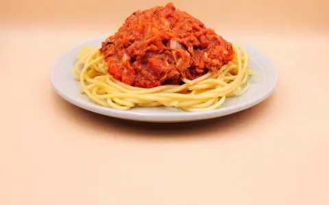 Porcja spaghetti z sosem pomidorowym i tuńczykiem, podana na jasnym talerzu.