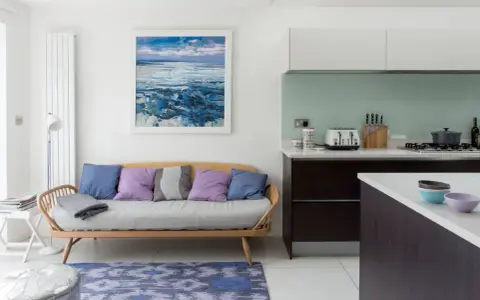 Acogedora cocina con un cómodo sofá de madera y cojines coloridos, junto a una isla y un cuadro de paisaje marino.