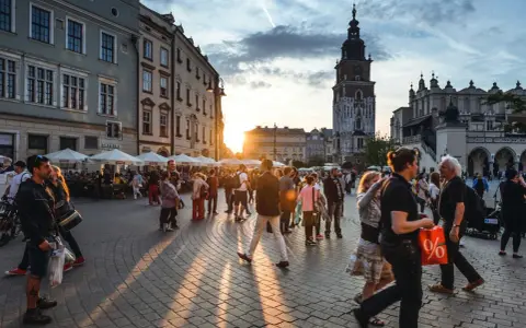 Tłum ludzi spaceruje po Rynku Głównym w Krakowie o zachodzie słońca. Widać Sukiennice i wieżę Ratuszową. Czy jest krakow safe? Tak, to tętniące życiem, bezpieczne miasto.