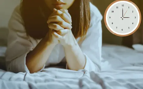 A woman is praying at 3am in the morning, her hands clasped tightly. The clock shows the early hour.