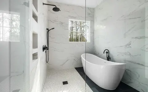 Salle de bain moderne avec baignoire îlot et douche vitrée, murs en porcelaine ou céramique effet marbre.