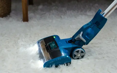 Blauer Staubsauger mit LED-Licht reinigt flauschigen Teppich. Die Leistung, wie viel Watt hat ein Staubsauger, ist entscheidend für die Saugkraft.