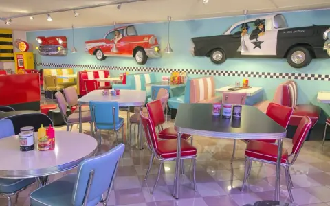 Interni di un diner in **stile americano** con sedili color pastello, tavoli cromati e decorazioni a tema auto d'epoca.