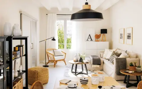 Acogedor salón estilo nórdico con sofá, sillón de mimbre, mesa de centro y estantería negra.