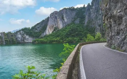 Strada panoramica lungo un lago verde smeraldo, con imponenti pareti rocciose e vegetazione lussureggiante. Un percorso suggestivo per raggiungere la baia di Bogn.