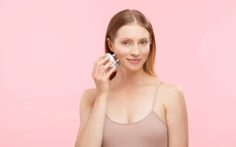 A woman demonstrates how to use a face massager on her cheek, showing a simple skincare routine.
