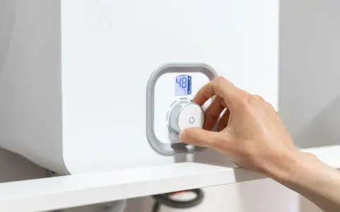Mano ajustando el dial de una caldera para bajar la presión. La pantalla digital muestra 48°C.