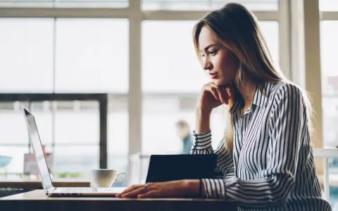 Donna pensa a come fare un webinar, seduta al laptop con una tazza di caffè.