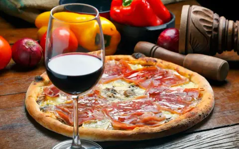 Idealne wino do pizzy, z kieliszkiem czerwonego wina i składnikami na pizze w tle.