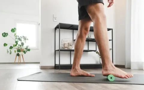 Mann rollt mit einem kleinen grünen Ball unter dem Fuß, um Plantarfasziitis-Hausmittel anzuwenden.