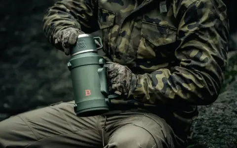 Mężczyzna w mundurze wojskowym trzyma termos. Dowiedz się, jak wyczyścić nakrętkę od termosu, by napój był zawsze świeży.