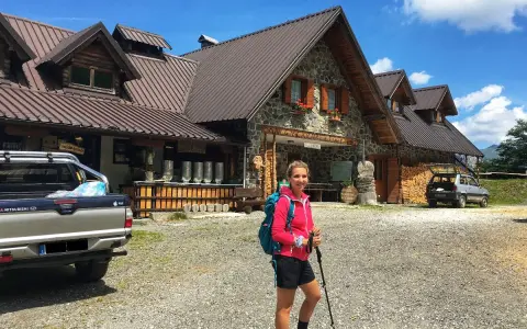 Ragazza con zaino e bastoncini da trekking davanti a un rifugio alpino, una delle tipiche malghe in Friuli.