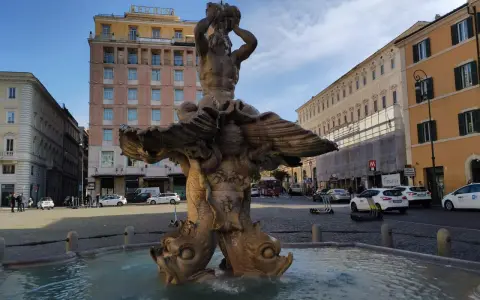 Fontana del Tritone in Piazza Barberini, Roma, con edifici storici e traffico sulla via dei Cappuccini.