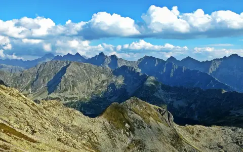 Widok z Zawratu na skaliste szczyty Tatr pod błękitnym niebem z białymi chmurami.