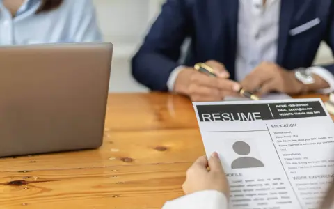 Osoba przegląda CV, na którym widnieje sekcja "Umiejętności twarde". Obok leży laptop.