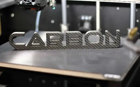 Ein 3D-Drucker fertigt das Wort "CARBON" aus einer Carbonplatte.