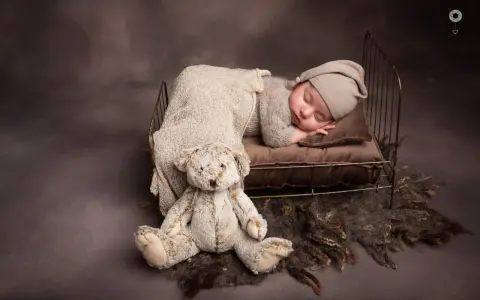 Dolce bimbo appena nato dorme sereno in una culla con un orsacchiotto. Foto bimbi appena nati.