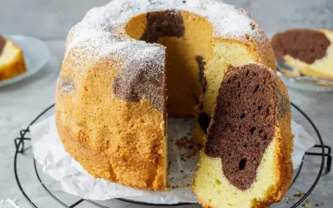 Saftiger Marmorkuchen, perfekt gebacken mit Ober-/Unterhitze oder Umluft, bestäubt mit Puderzucker. Ein Stück ist bereits angeschnitten.