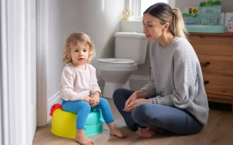 Mama uczy dziecko korzystać z nocnika. Mała dziewczynka siedzi na kolorowym nocniku, a mama siedzi obok, wspierając ją.
