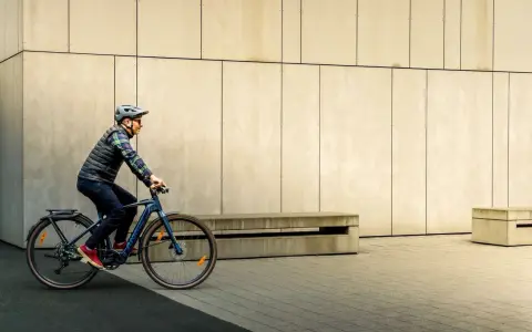 Mężczyzna w kasku i kamizelce jedzie na rowerze typu fitness w miejskim otoczeniu.