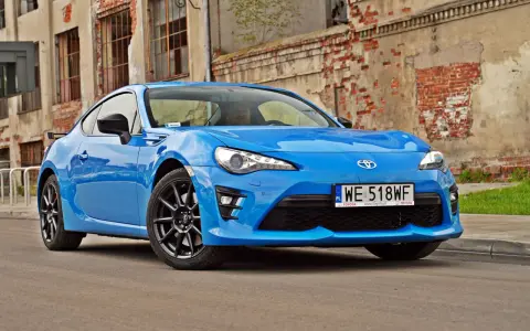 Błękitna Toyota GT86, znana też jako Toyota BRZ, zaparkowana przed zniszczonym budynkiem.