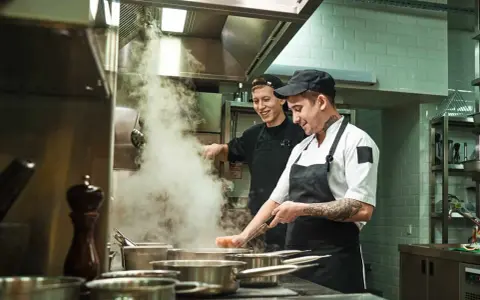 Deux chefs travaillent dans une cuisine de restaurant, respectant la norme de qualité. Vapeur s'échappant des casseroles.