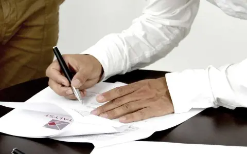 Mężczyzna podpisuje dokumenty, stając się ubezpieczającym dla ubezpieczonego. Na papierze widoczne logo firmy.