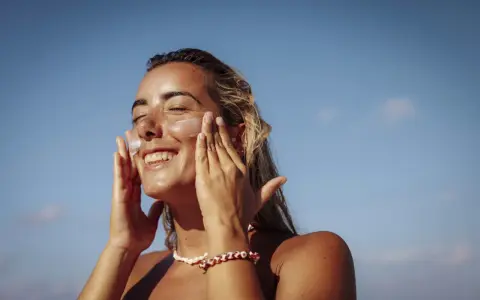 Donna sorridente applica crema solare per proteggere la pelle da macchie e tumore.
