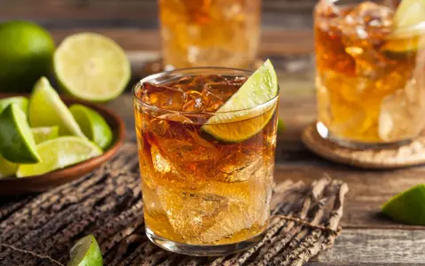 Orzeźwiający drink z whisky i coca colą, ozdobiony plasterkiem limonki. Obok miseczka z kawałkami limonki.