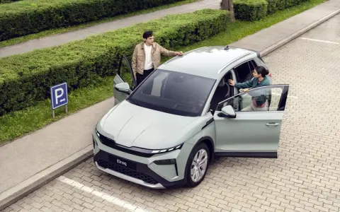 Jasnoszary elektryczny SUV Škoda Elroq z otwartymi drzwiami, obok którego stoją młoda kobieta i mężczyzna.