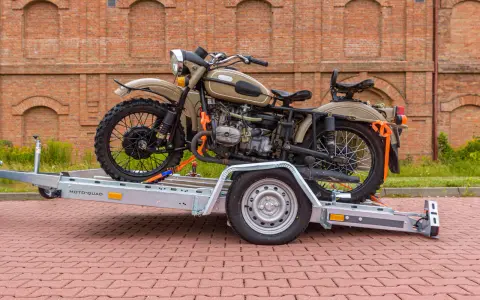 Motocykl Ural zabezpieczony pasami na przyczepie, pokazujący, jak przewieźć motocykl na zwykłej przyczepie.