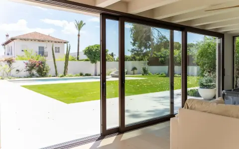 Amplias puertas correderas de cristal conectan el interior con un jardín con piscina, permitiendo una ventilación natural y la entrada de luz.