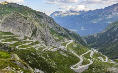 Strada tortuosa che sale sul passo Austria, circondata da montagne verdi e rocce imponenti.