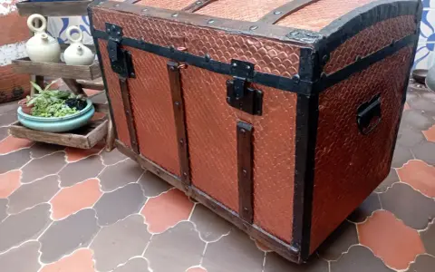 Un baúl antiguo restaurado, con detalles metálicos y acabado en cobre texturizado, listo para guardar tesoros.