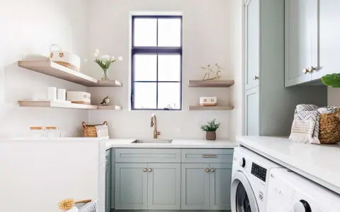 Stylish laundry room with mint cabinets, floating shelves, and a sink. This organized space shows how to organize laundry room with baskets and jars.