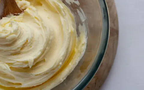 Une cuillère en bois mélange une crème au beurre traditionnelle onctueuse dans un bol en verre.