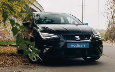 Coche negro SEAT León FR aparcado entre hojas secas y un muro de ladrillos. El emblema "FR" indica su versión deportiva.