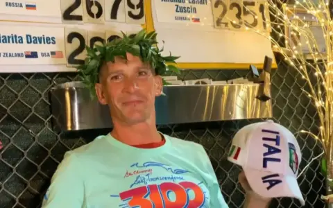 Vincitore con corona d'alloro, indossa una maglietta con scritto "3100" e un cappellino "ITALIA". Potrebbe essere un traguardo della ultramaratona più lunga del mondo.