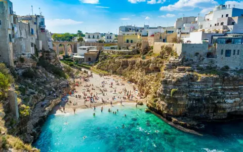 Słoneczne bari plaże w Apulii, z turkusową wodą i białymi domami na klifach. Ludzie odpoczywają na piasku i kąpią się w morzu.