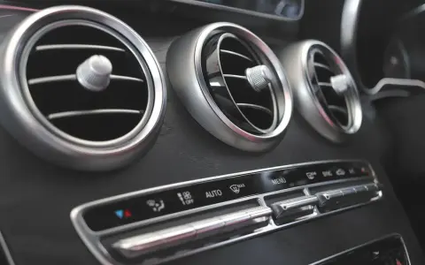 Trzy okrągłe nawiewy wentylacji w samochodzie, z pokrętłami do regulacji. Poniżej panel sterowania klimatyzacją, z przyciskami AUTO i MAX. Czekam na bardzo gorące powietrze z nawiewu.