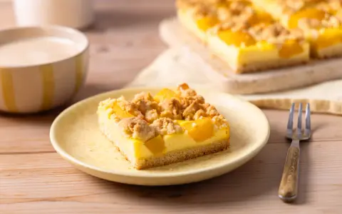 Ein Stück saftiger Pfirsich Blechkuchen mit Vanillepudding und Streuseln auf einem gelben Teller, daneben eine Gabel.
