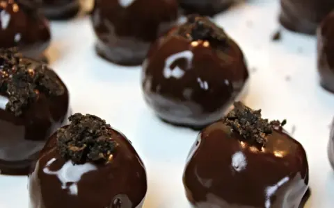 Deliziosi tartufini al cocco ricoperti di cioccolato fondente lucido, guarniti con briciole croccanti.